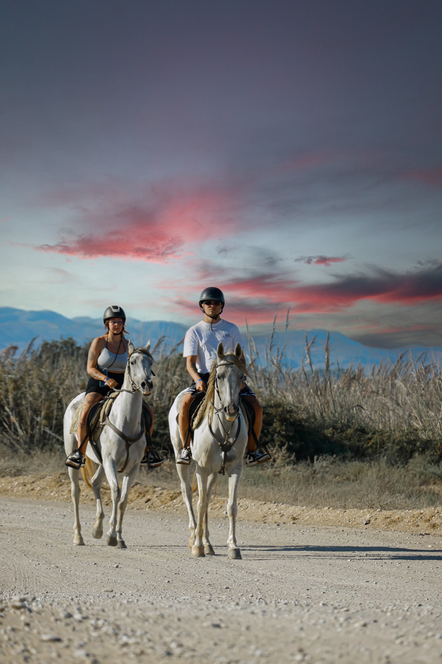 Two riders on the beach beneath a rose evening sky